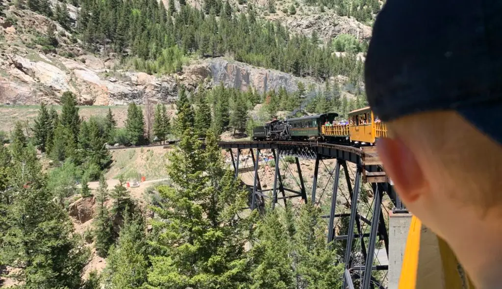 A boy is having an adventure with his family, looking at the Georgetown Loop train on a bridge.