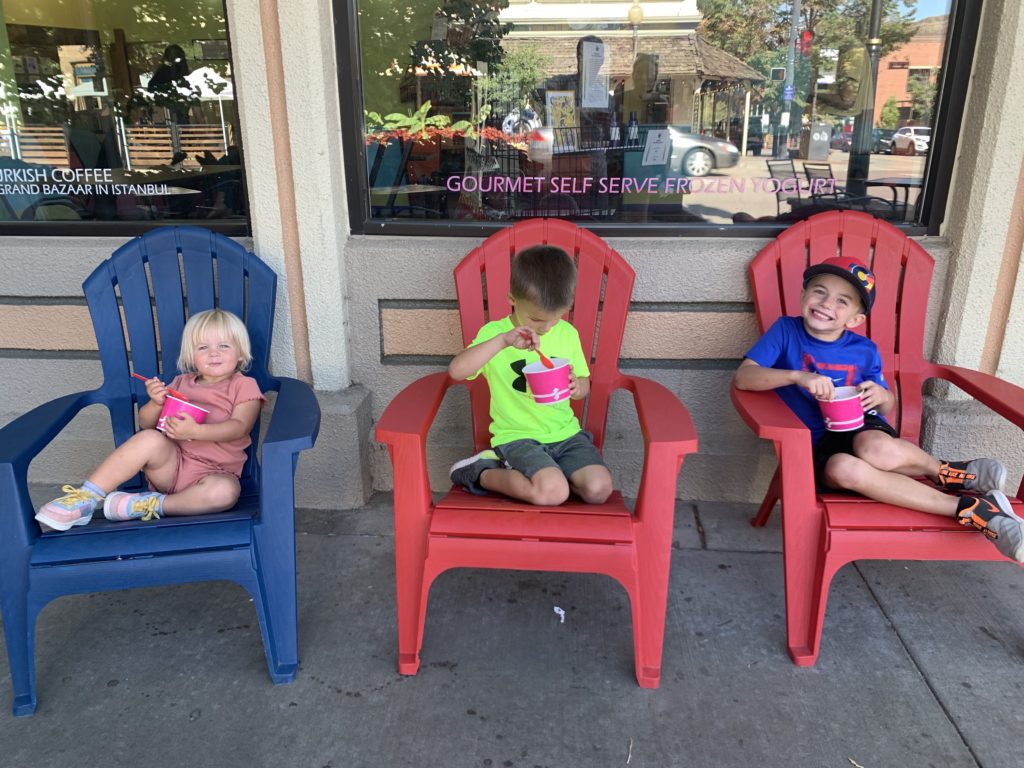 Three adventurous kids enjoying a family outing while sitting in adirondack chairs in front of a store.