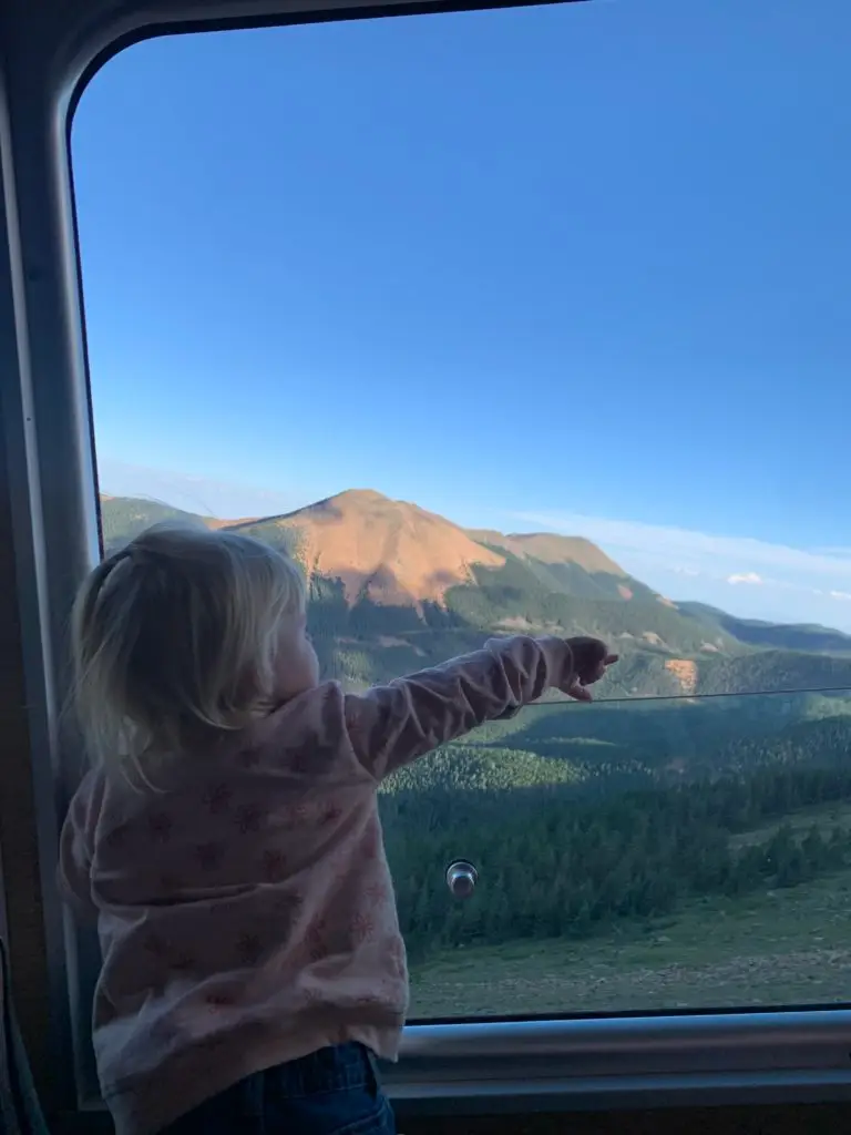 A little girl pointing out the window of a train.