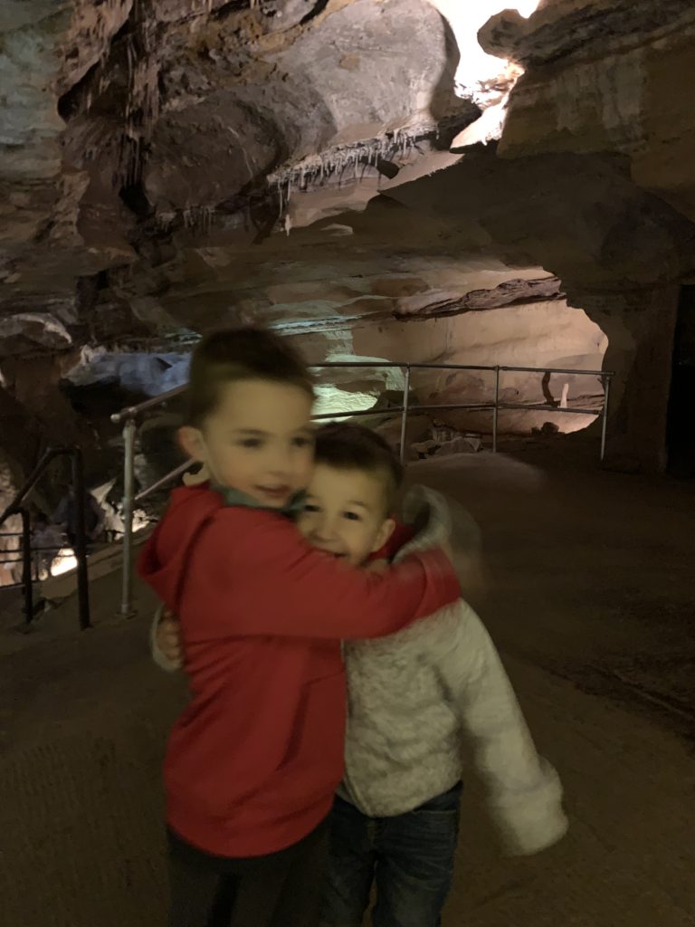 Two boys hugging in front of a cave.