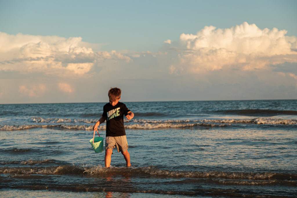 A boy is standing in the ocean holding a bucket on a Hilton Head family vacation.