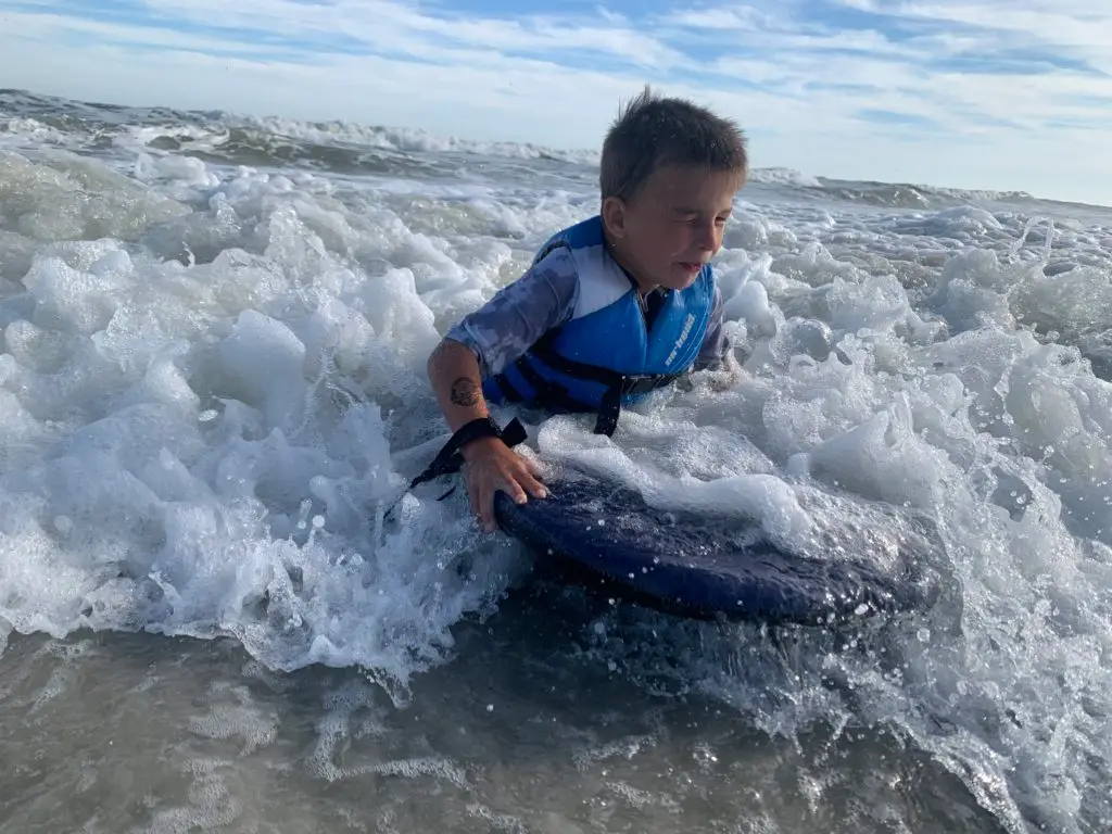 A young boy riding a surfboard in the ocean.  Great beach activities for kids.