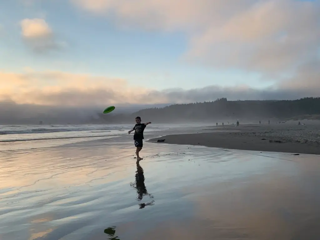 A boy is playing frisbee on the beach.  perfect for beach activities for kids.