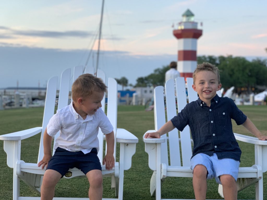 Two boys sitting in white chairs in front of a lighthouse on their Hilton Head family vacation.