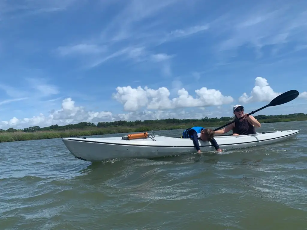 A mom is paddling a white kayak in the water with her son on a Hilton Head family vacation.