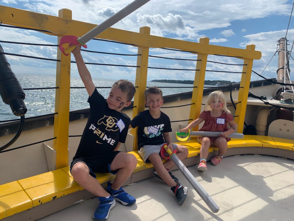 Three children sitting on the deck of a sailboat on a Hilton Head family vacation.