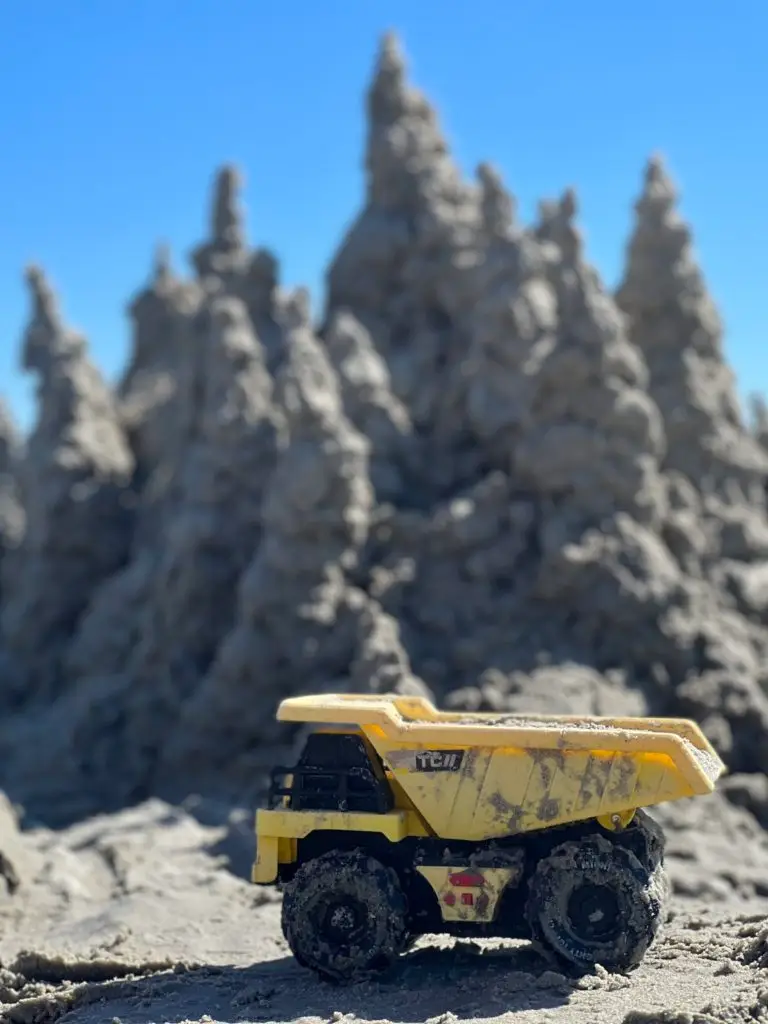 A toy dump truck sits on top of a pile of sand.