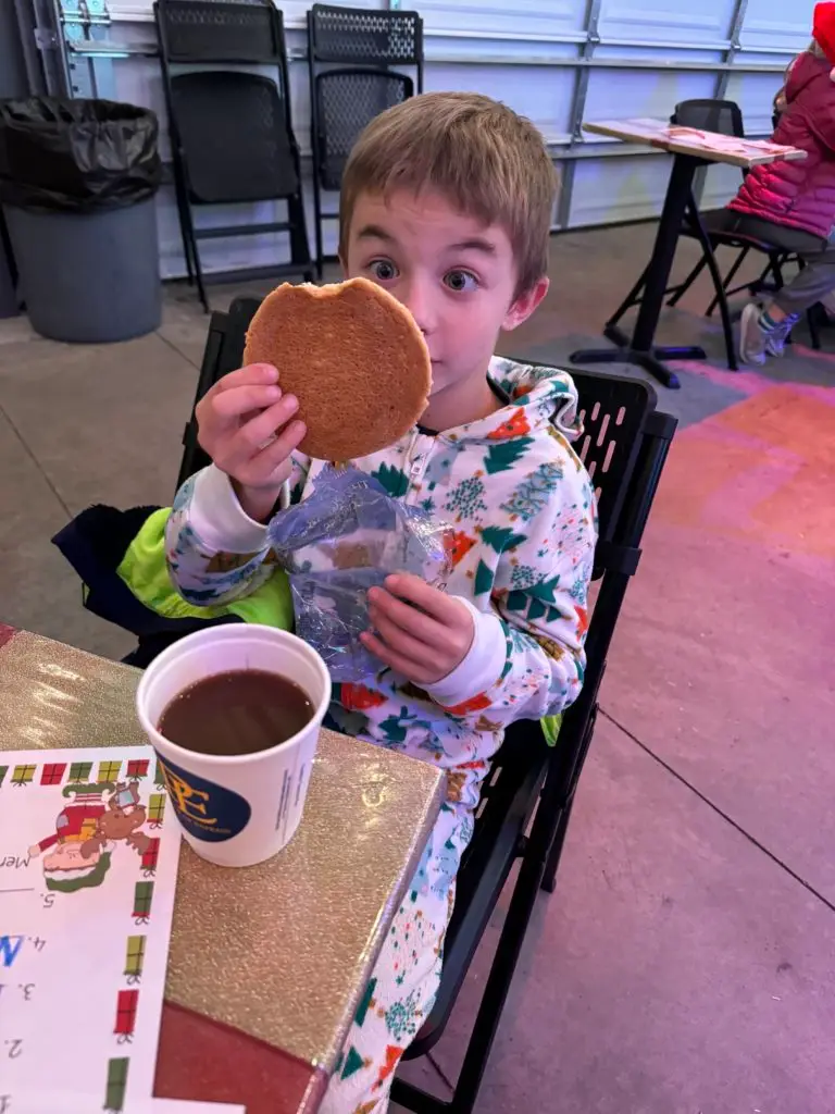 A boy in pajamas eating a cookie in front of a table on the Polar Express train ride.