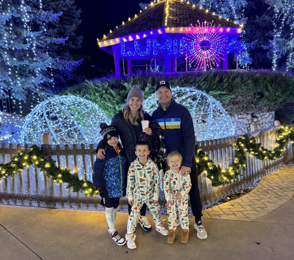 A family in pajamas standing in front of a gazebo with christmas lights.