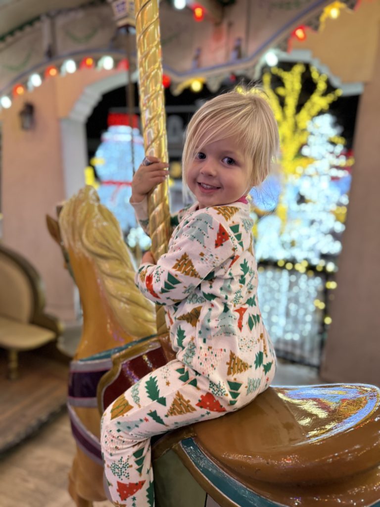 A little girl riding a carousel in a christmas pajamas.