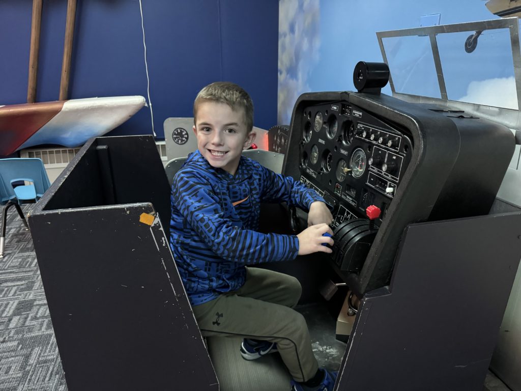 A young boy sitting in an airplane simulator at Wings Over The Rockies With Kids.