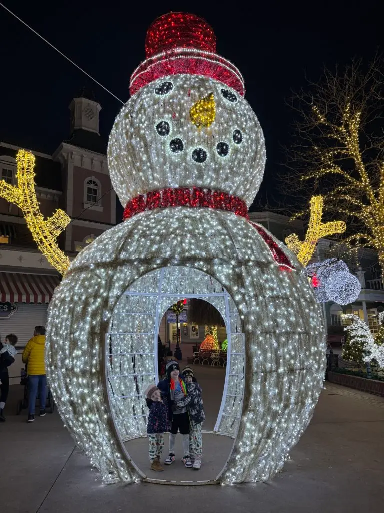 A snowman decorated with lights in front of a building.