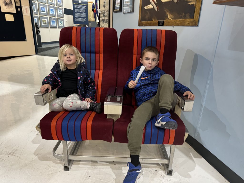 Two children sitting on airplane seats in a the museum Wings Over The Rockies With Kids