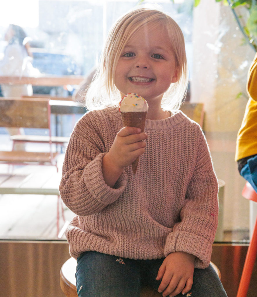 A little girl sitting on a stool eating an ice cream cone at Jeni's Splendid Ice Creams in Beverly Hills.  Beverly Hills With Kids. 