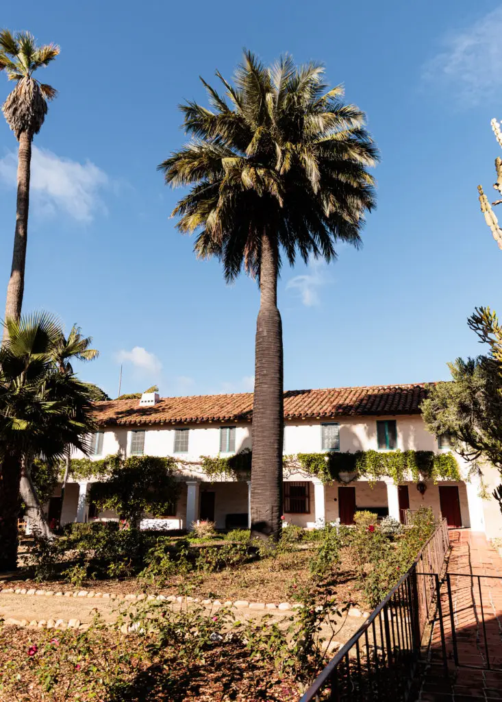 A palm tree in front of a house.  Old Mission Santa Barbara with kids.