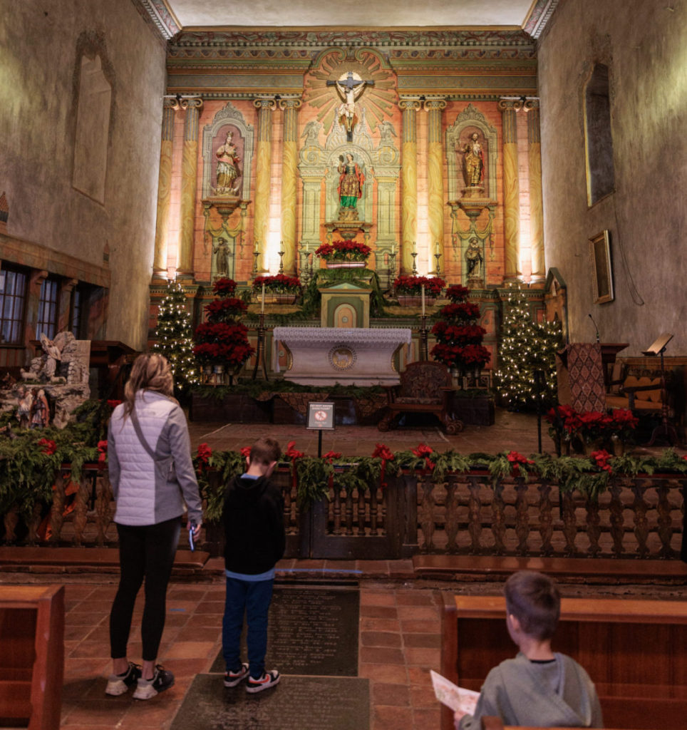 A man and a woman standing in front of a church.  Old Mission Santa Barbara with kids.