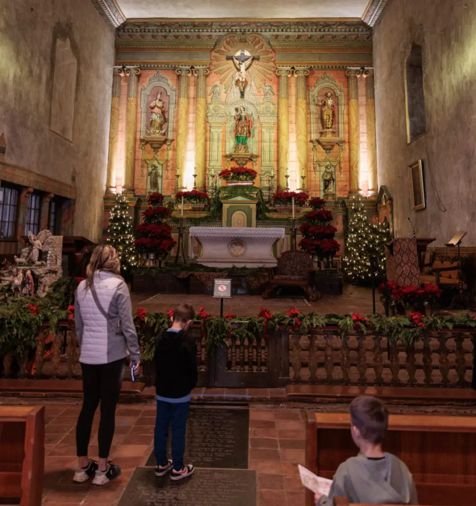 A man and a woman standing in front of a church.  Old Mission Santa Barbara with kids.