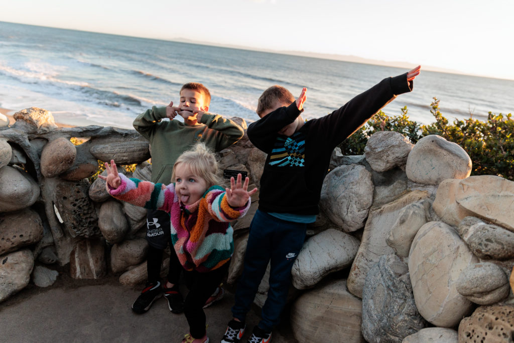 A group of kids on a rock wall in front of the ocean. Beaches in Santa Barbara With Kids