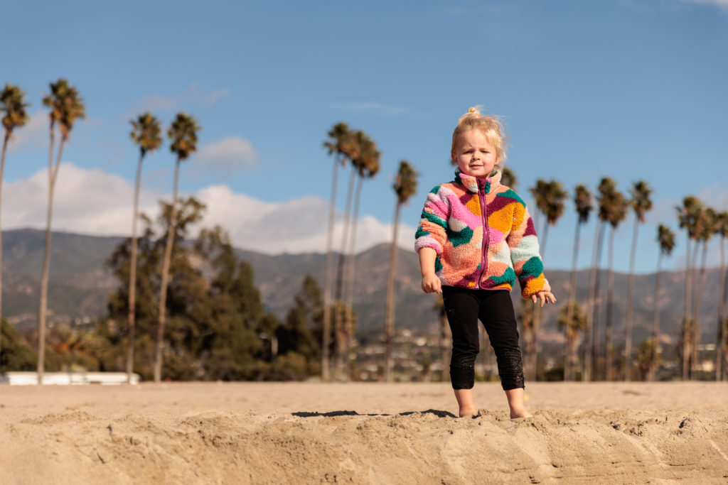 A little girl standing in the sand with palm trees in the background. Beaches in Santa Barbara With Kids