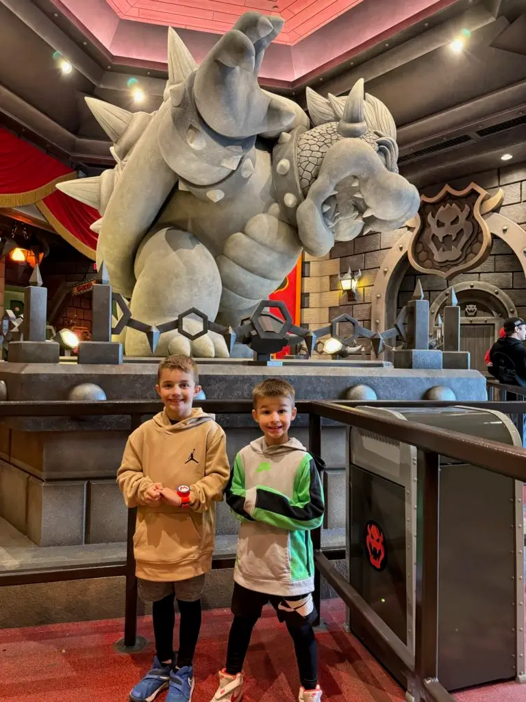 Two boys standing in front of a giant statue of a nintendo character for our Super Nintendo World review
