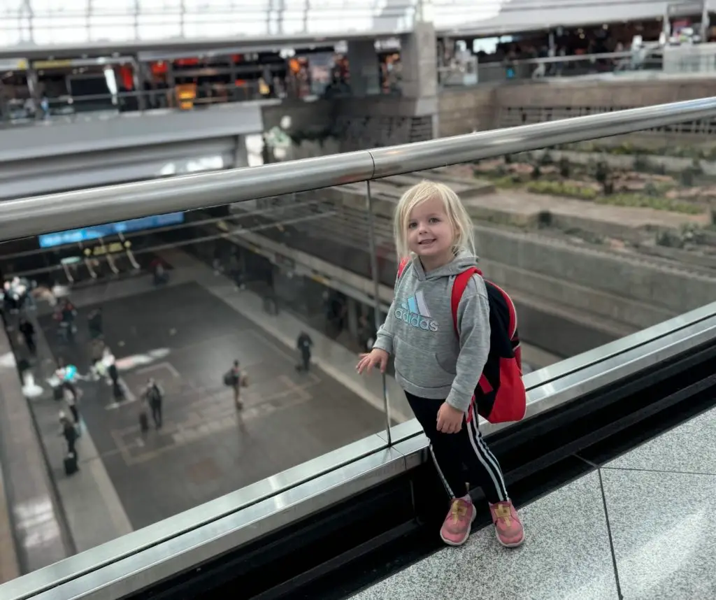 A little girl standing in an airport with a backpack.  Is Clear worth it for families.