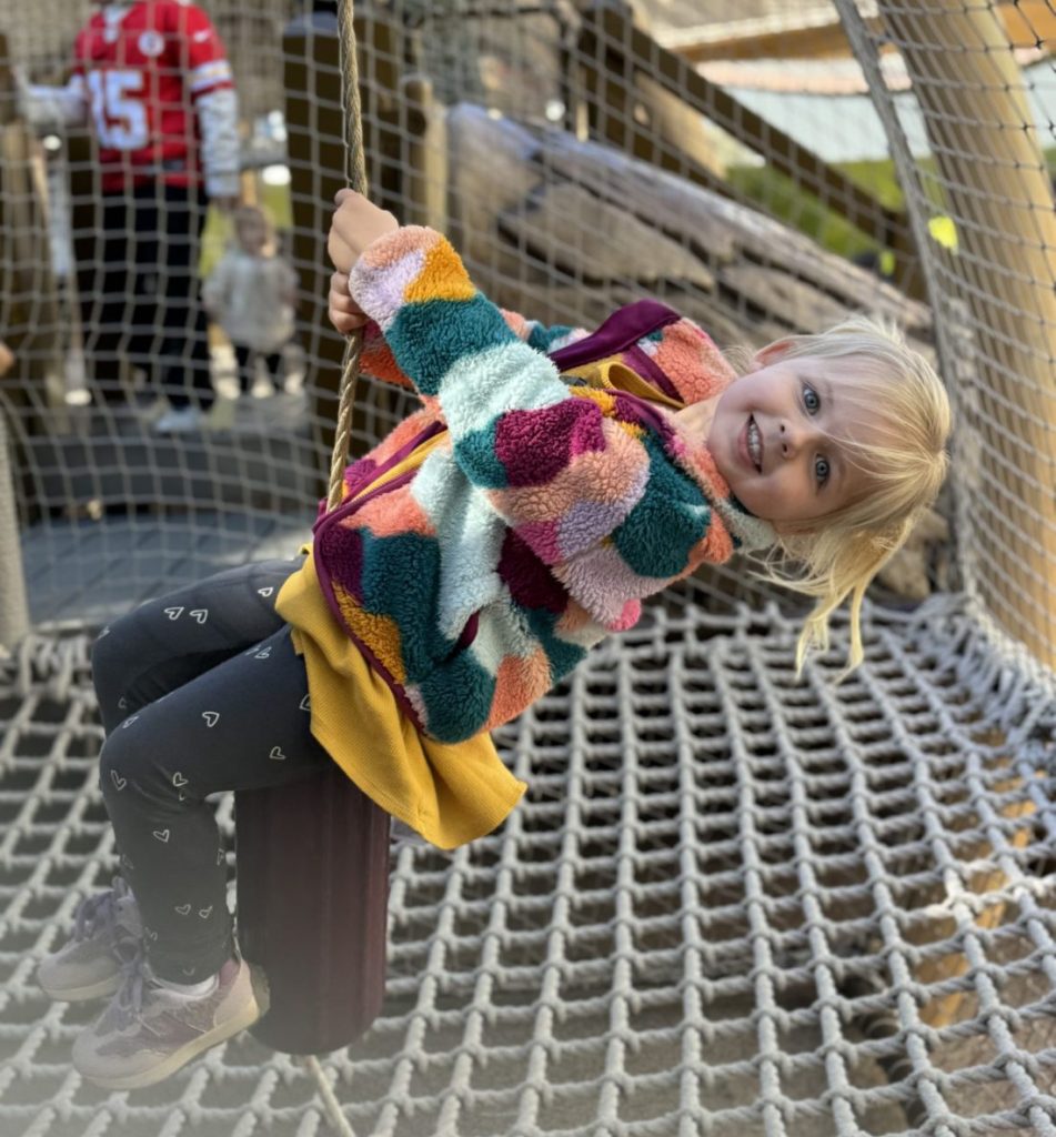 A little girl is swinging on a swing at a playground. Universal Studios Hollywood with Kids