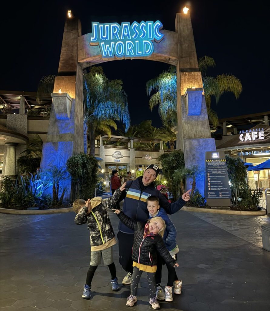 A family posing in front of the entrance to jurassic world.  Universal Studios Hollywood with Kids