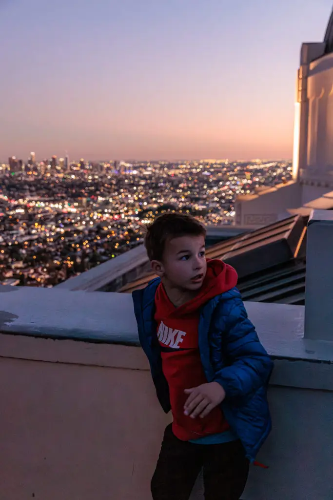 A boy is standing on a ledge overlooking a city.  Griffith Observatory with kids