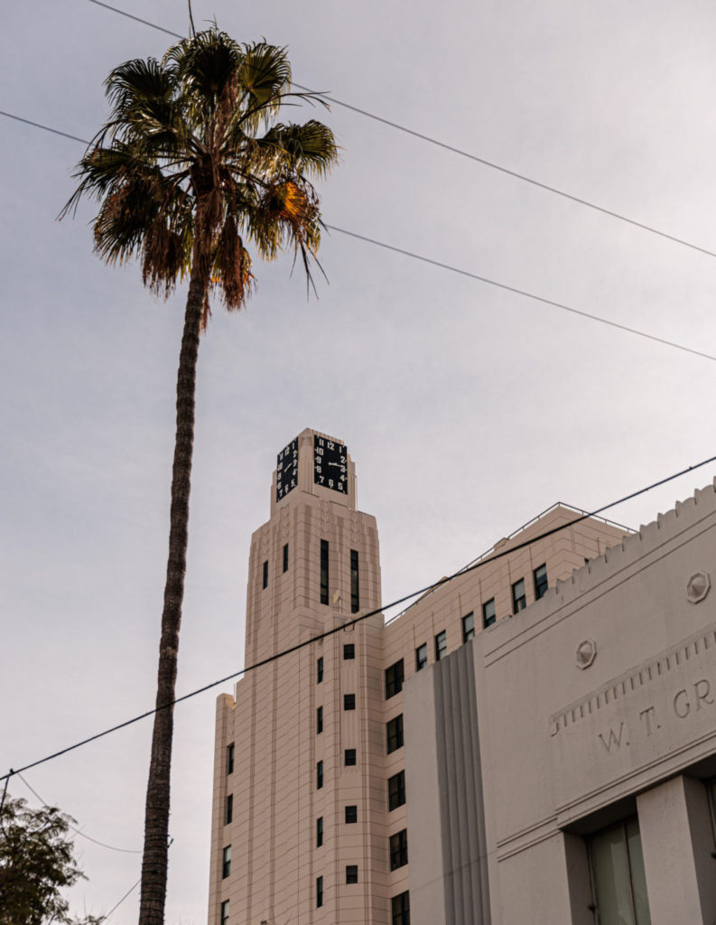 A building with a clock tower and a palm tree. 3rd Street Promenade with kids