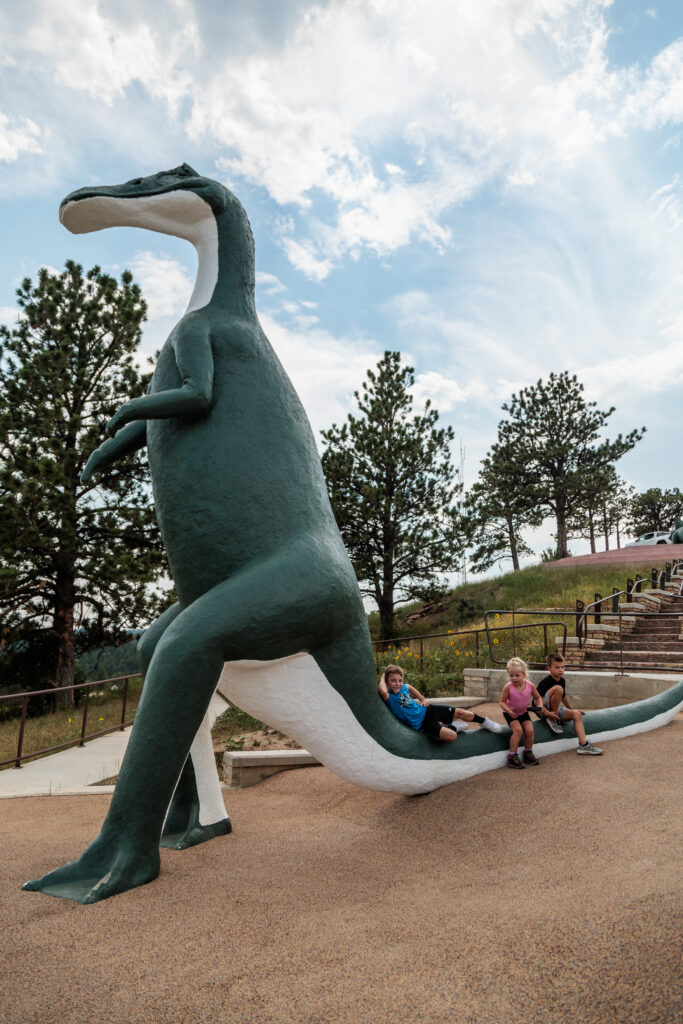 Three kids on a dinosaur statue at Dinosaur Park in Rapid City.  Free things to do in Rapid City with kids.