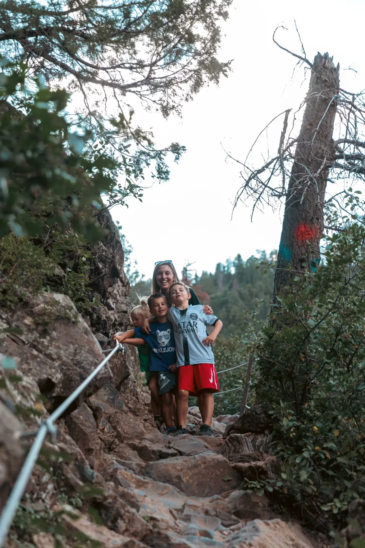 A woman and two children stand on a rocky hiking trail, surrounded by trees. 2 days in Ouray with kids.