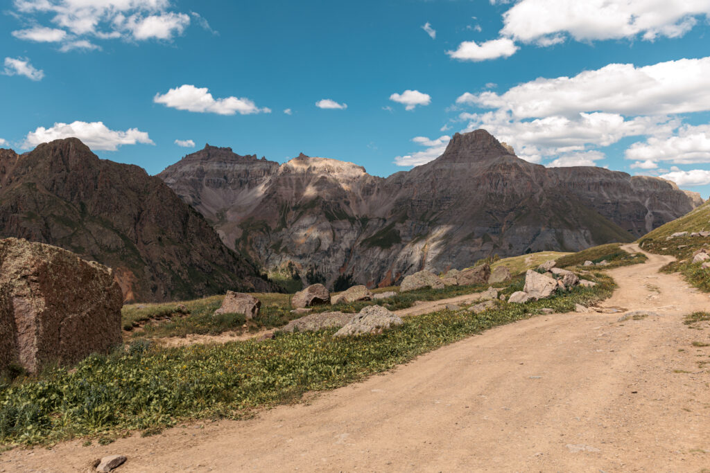 Dirt path leading into a mountainous landscape with rocky peaks under a blue sky with scattered clouds. 2 days in Ouray with kids.