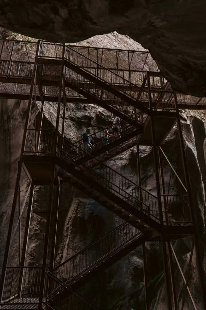 A metal staircase inside a cavern, with people ascending. Rocks and natural lighting create a dramatic atmosphere.  2 days in Ouray with kids.