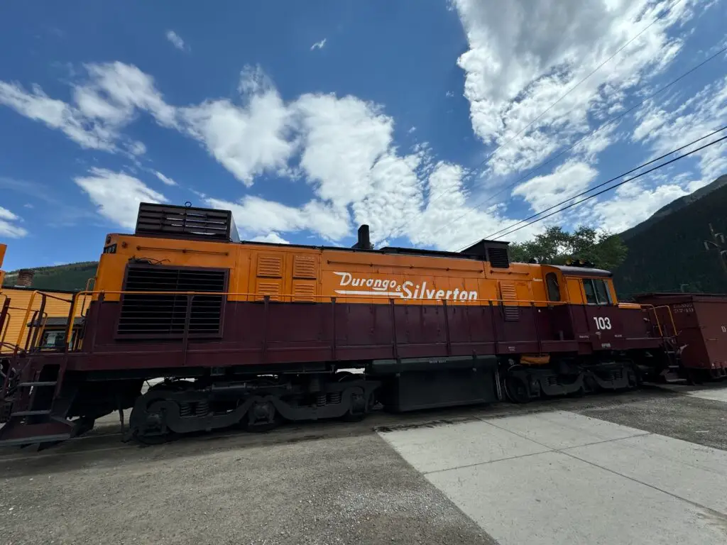 Orange and maroon Durango & Silverton train locomotive numbered 103 on a clear day.  Afternoon in Silverton with Kids.