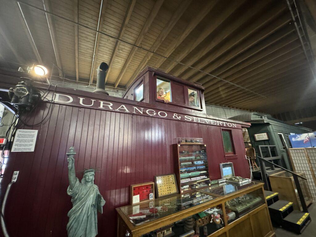 Historic train car display labeled "Durango & Silverton" with memorabilia cases and a small Statue of Liberty replica inside a museum.  durango train with kids.