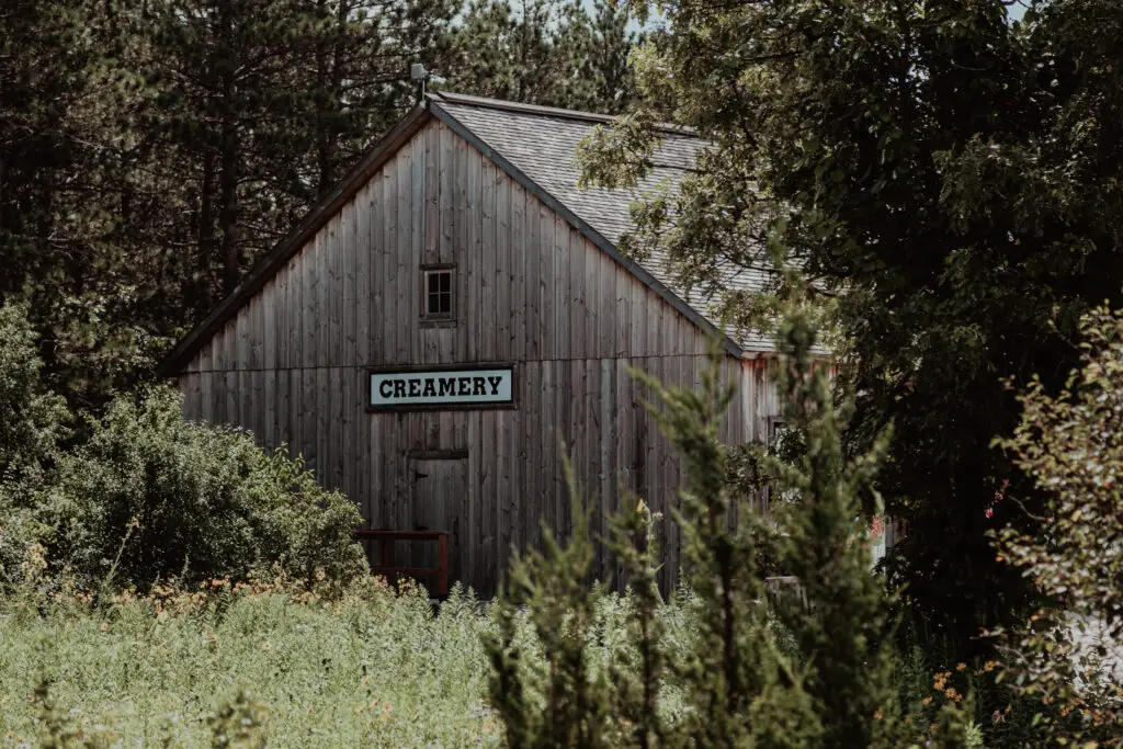 A rustic wooden creamery building surrounded by dense greenery and trees.  Old World Wisconsin with Kids.