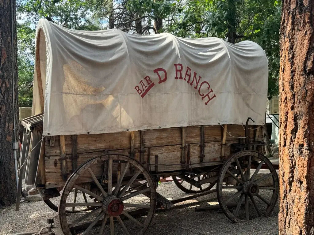 Wooden covered wagon with "Bar D Ranch" on canvas, parked among trees.  Bar D Chuckwagon Suppers with kids