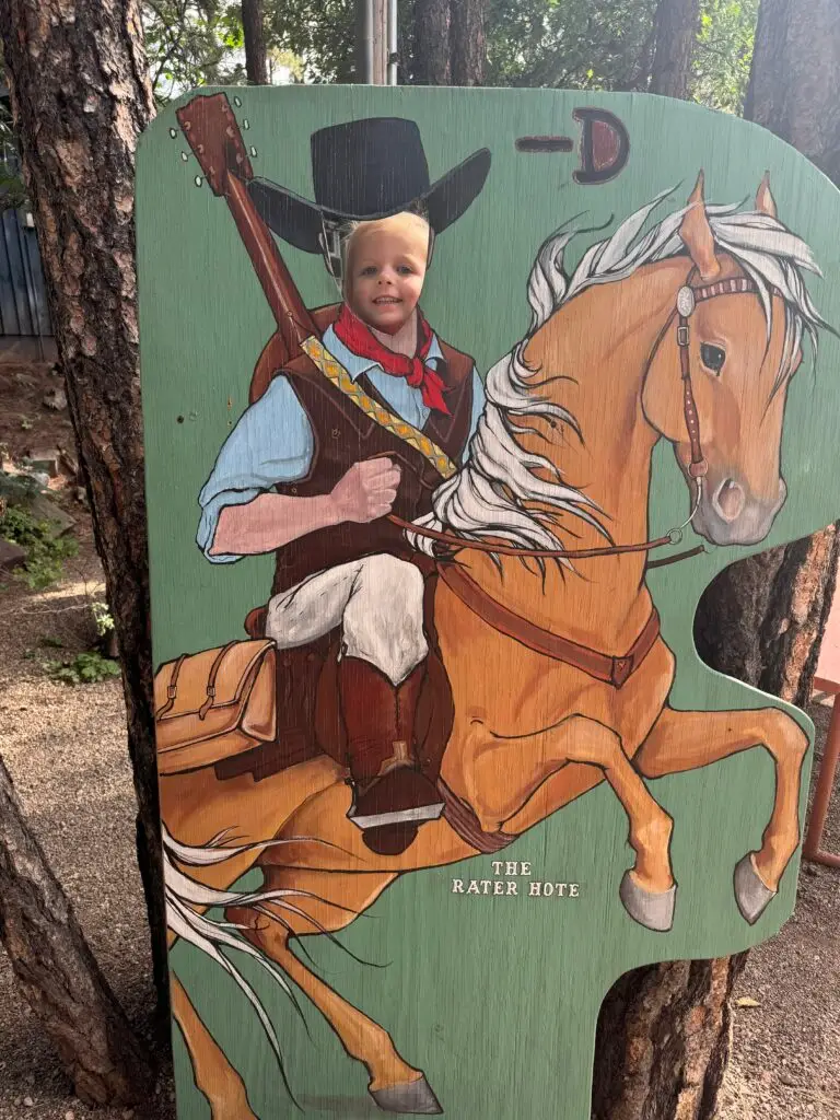 Child posing behind a wooden cutout of a cowboy on a horse, with their face in place of the cowboy's face.  Bar D Chuckwagon Suppers with kids