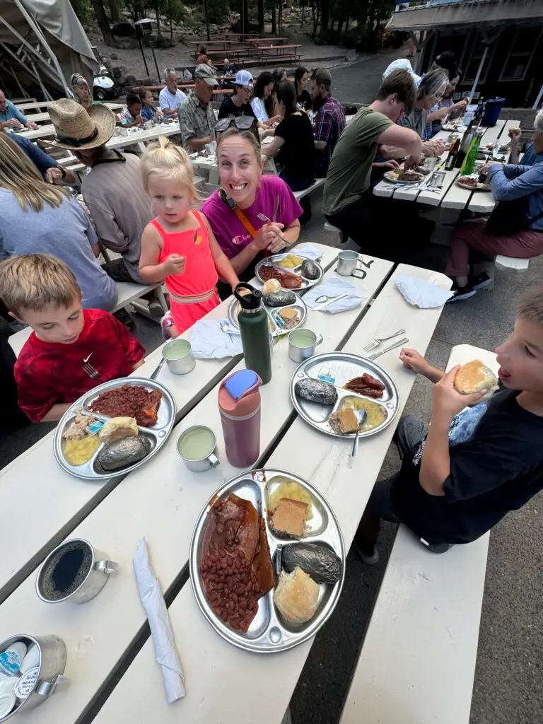 People sitting at an outdoor picnic table enjoying a meal with plates of food, including beans, rolls, and sausages.  Bar D Chuckwagon Suppers with kids