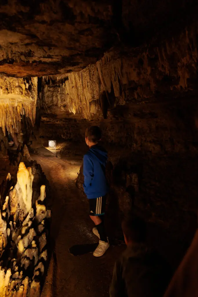 Child in blue jacket exploring a dimly lit cave with stalactites and stalagmites.  Cave of the Mounds with kids.