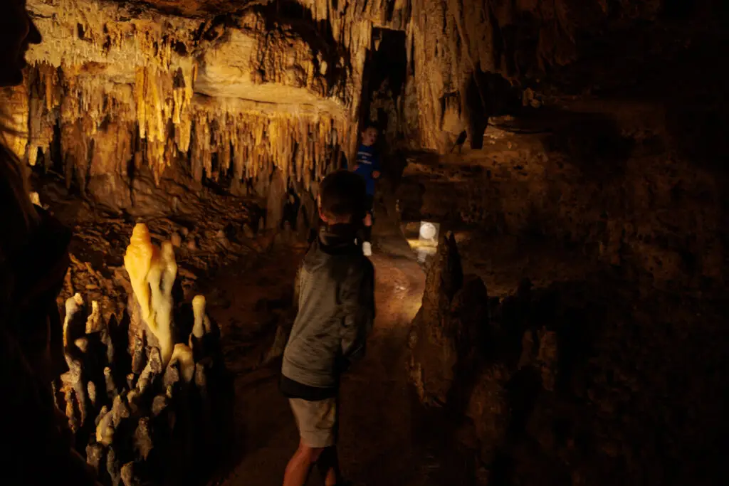 A group of people walking through a dimly lit cave with stalactites and stalagmites.  Cave of the Mounds with kids.