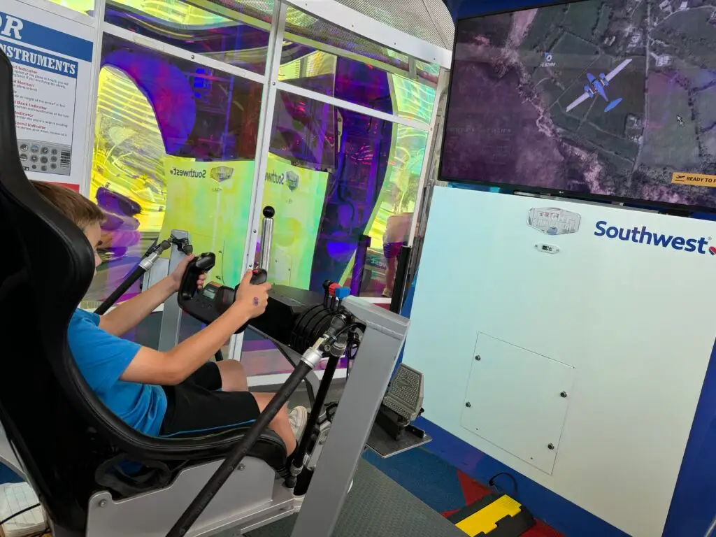 A person is using a flight simulator with joysticks, seated in front of a large screen displaying a plane.