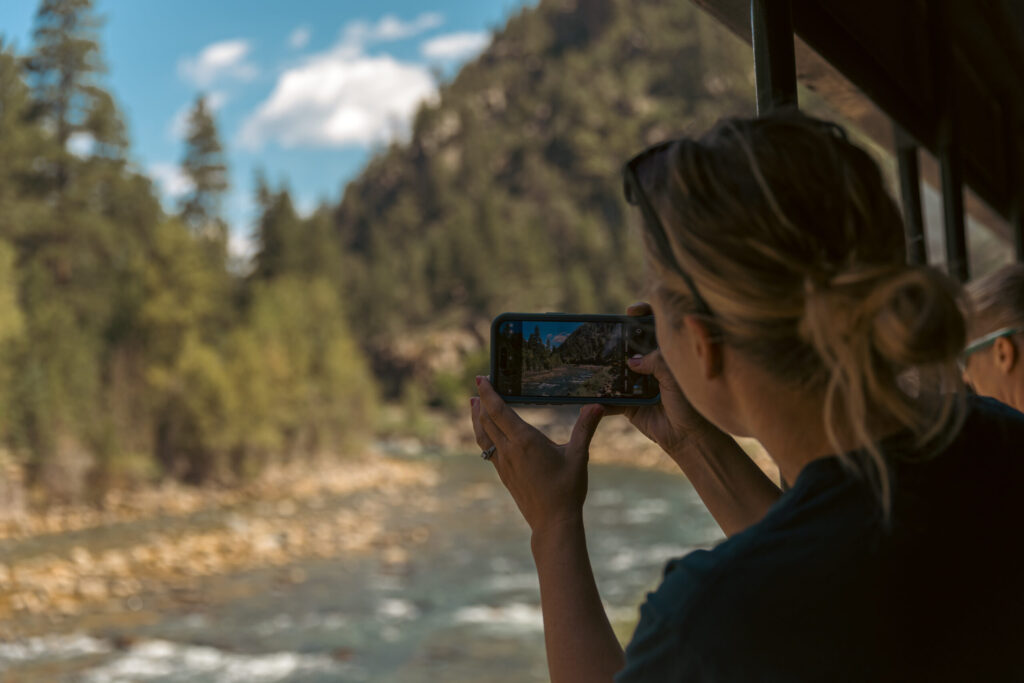 While aboard the historic Durango train with kids, a passenger captures a stunning photo of a scenic landscape featuring lush trees and a flowing river, all from the comfort of their seat as the vintage locomotive glides through nature's vibrant tapestry.