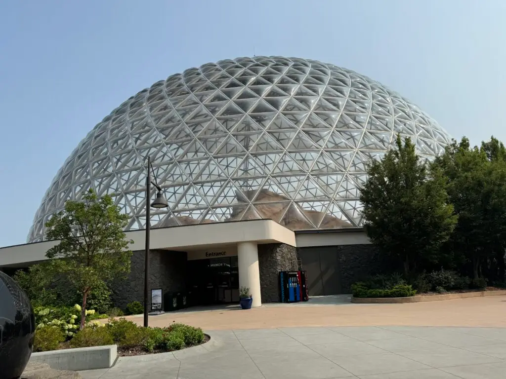 Geodesic dome structure with a glass and metal lattice, surrounded by trees, with an entrance labeled "Entrance" at the base.  Omaha Zoo with kids.