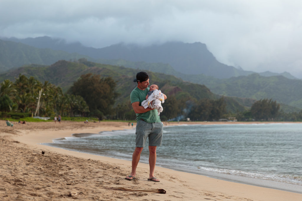 Family travel site photo of a man enjoying a family adventure on a beach with his baby in Hawaii.