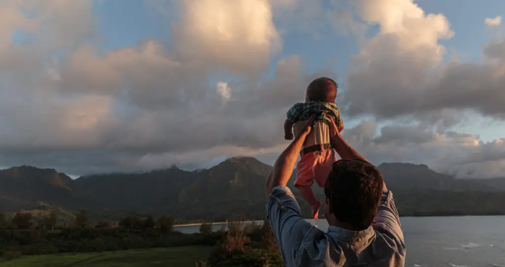 A man embracing his child on a family vacation by the ocean.