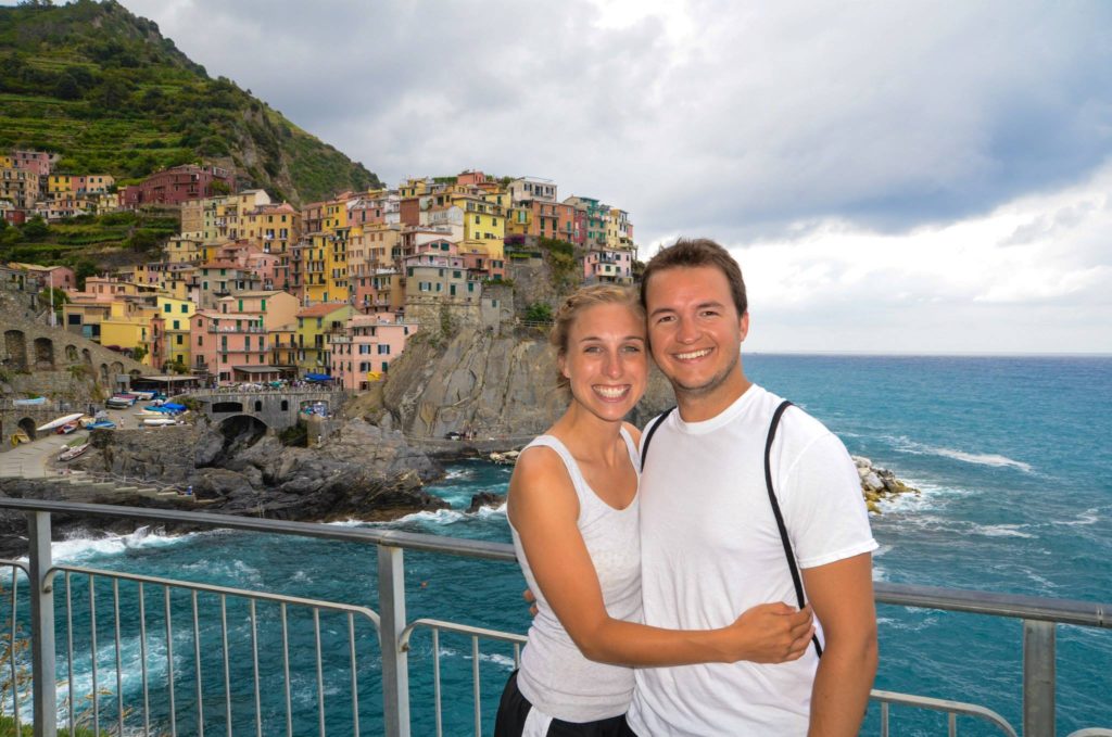 A couple adventuring and posing for a photo in front of a cliff overlooking the sea.