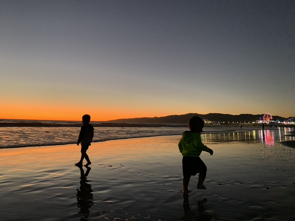 With warm destination ideas in mind, two kids are having an adventurous time at sunset on the beach in Santa Monica, CA.