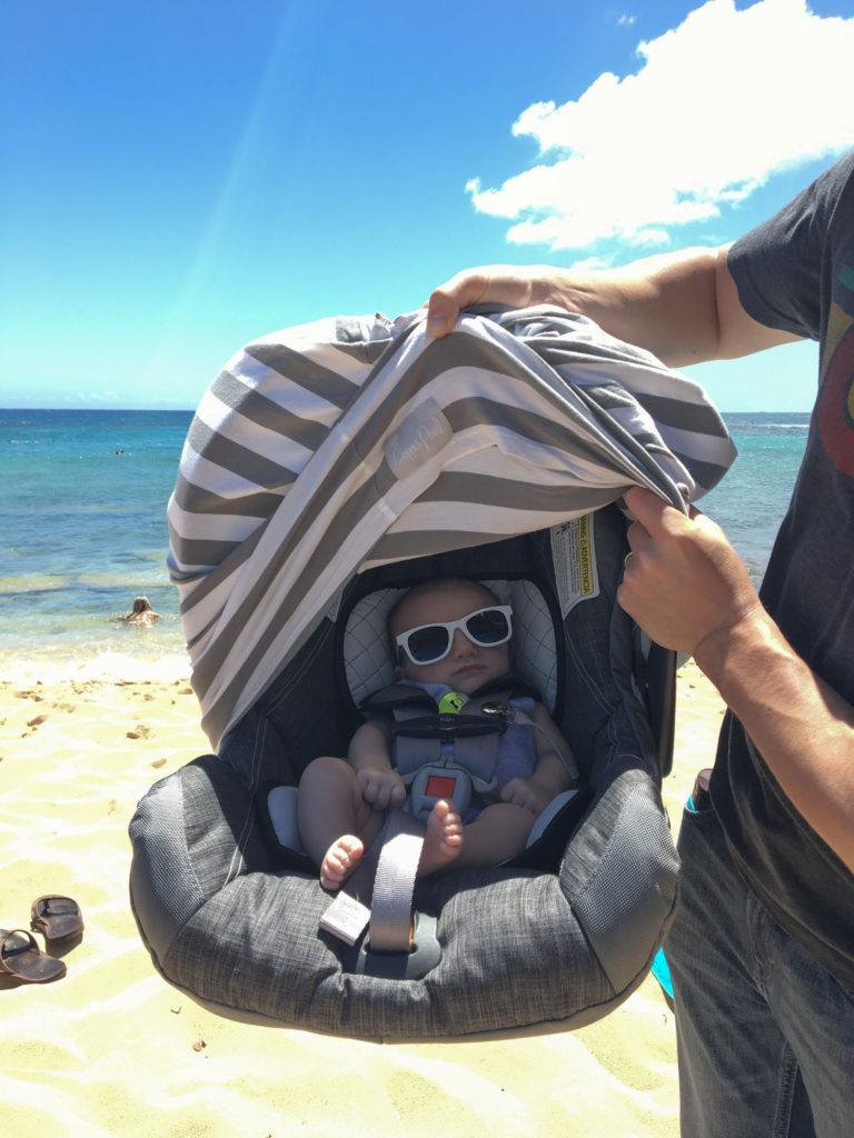 A man with a baby in a car seat enjoying an adventurous day at the beach.  A fun day can be had traveling with your baby. 