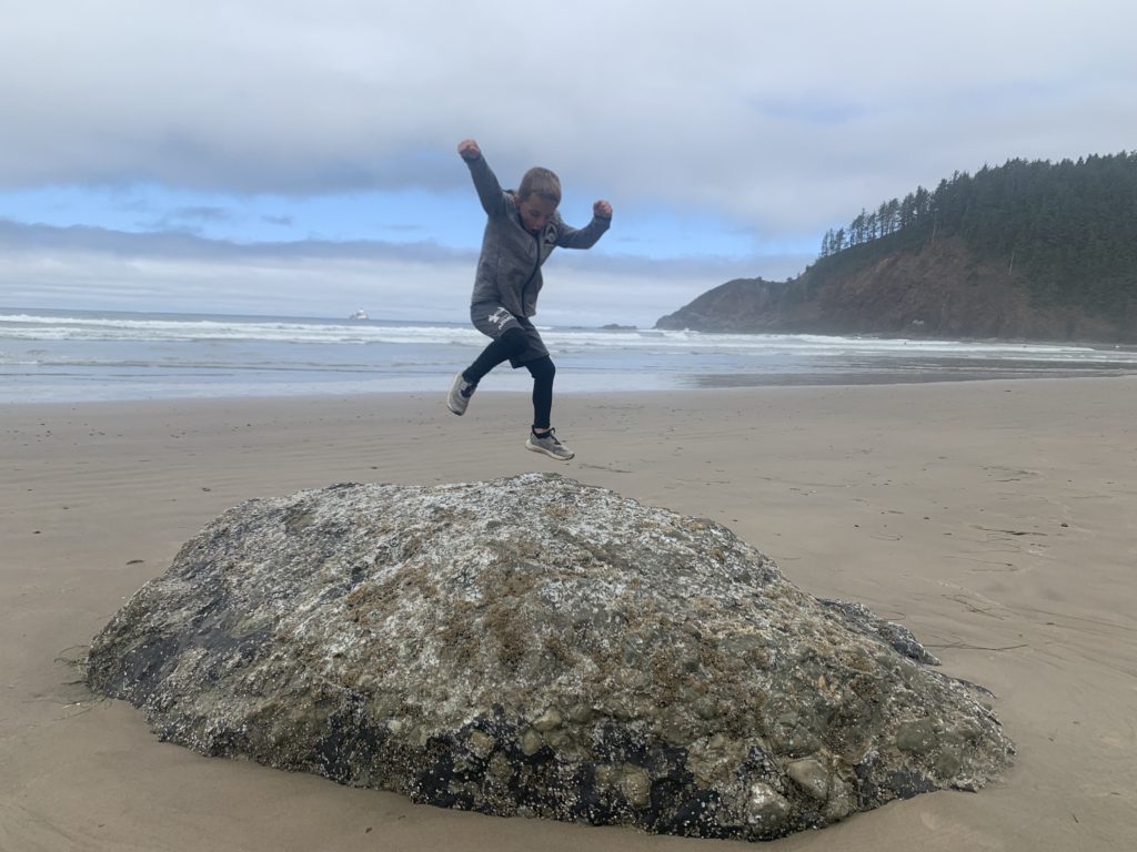 A family adventuring on the beach, with a boy jumping on top of a rock.